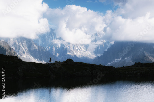 Silhouette of trail running woman in French Alps near Chamonix, with mountains and clouds in background, reflection on lake Lac de Cheserys in foreground