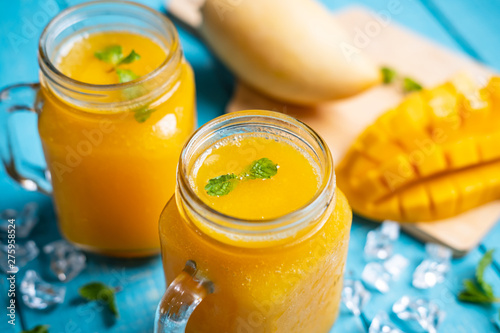 Refreshing mango smoothies in glass with ripe mango on wooden table