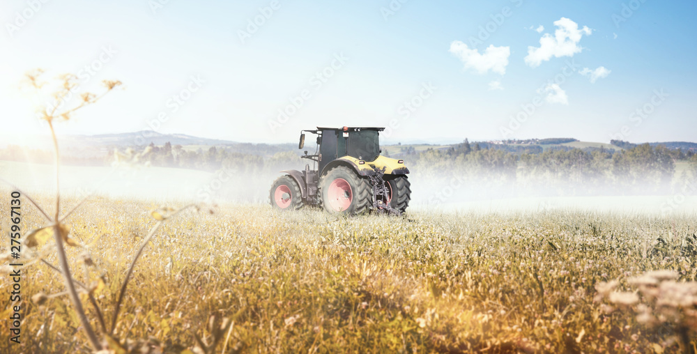 Fototapeta premium Traktor fährt über ein Feld bei Sonnenschein