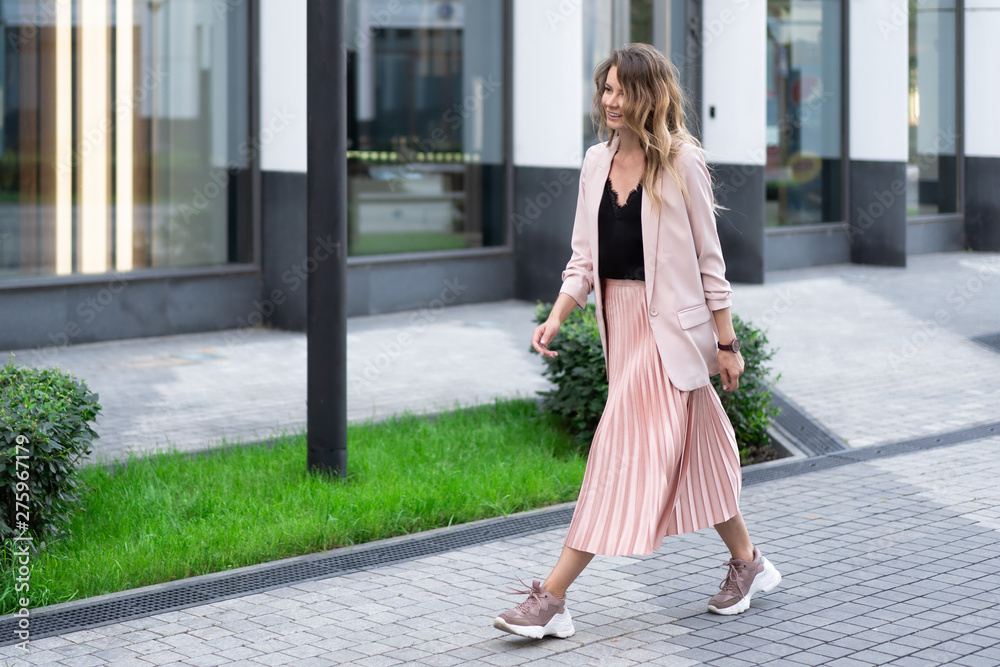 a girl in a peach jacket, a plush skirt and sneakers is walking along a stone street with a great mood. On the territory of a modern residential complex. a girl in a peach jacket, a plush skirt and sneakers is walking along a stone street with a great mood. On the territory of a modern residential complex.