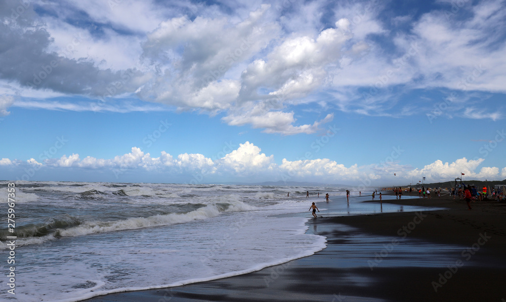 Vista della spiaggia di sabbia con le onde del mar Tirreno e cielo nuvoloso. Italia