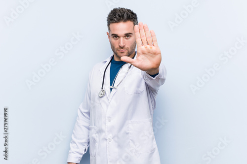 Young handsome doctor man standing with outstretched hand showing stop sign, preventing you.