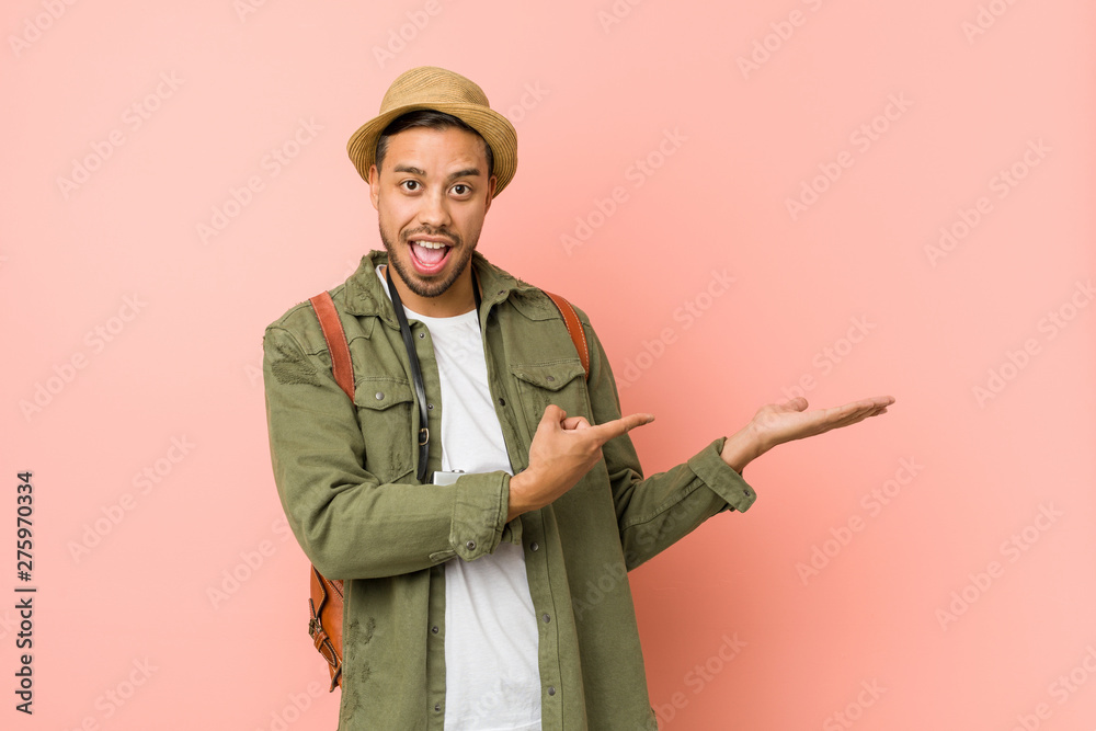 Young filipino traveler man excited holding a copy space on palm. Young filipino traveler man excited holding a copy space on palm.