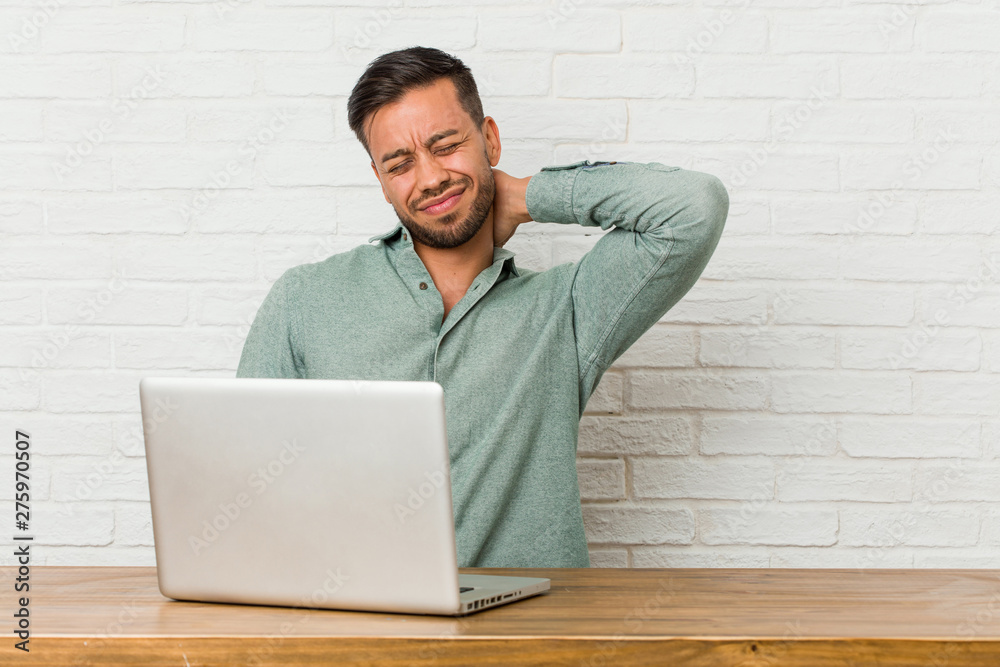 Young filipino man sitting working with his laptop suffering neck pain due to sedentary lifestyle. Young filipino man sitting working with his laptop suffering neck pain due to sedentary lifestyle.