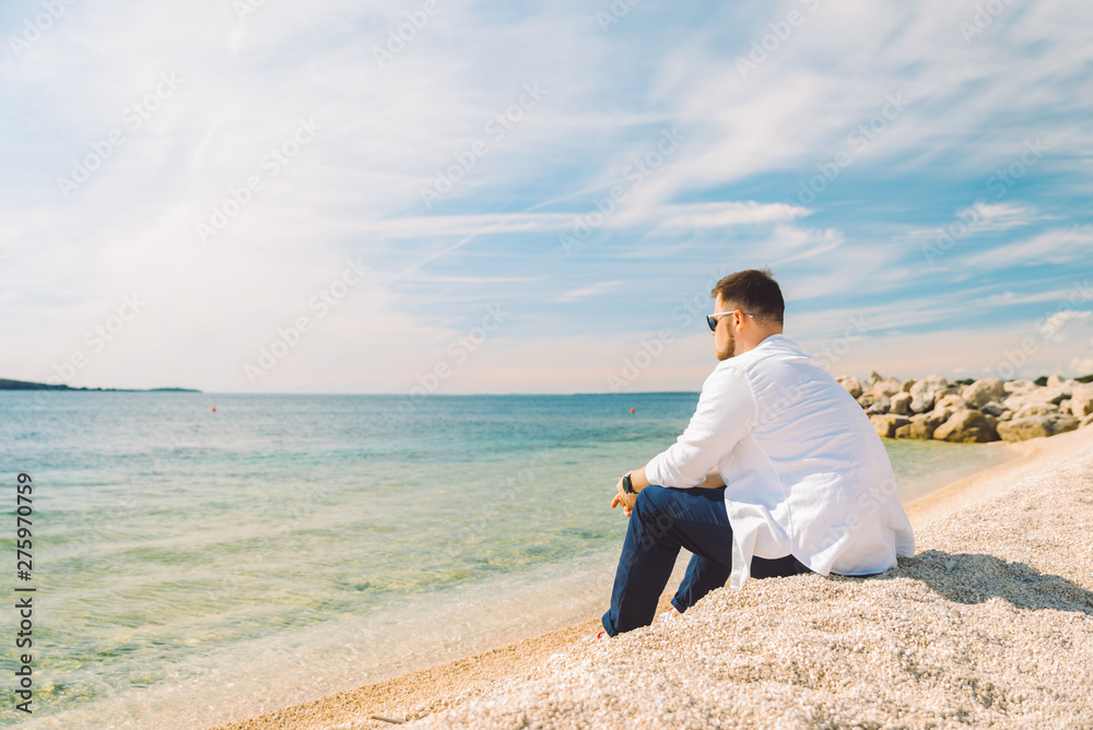 young stylish man sitting at sea beach enjoying the view