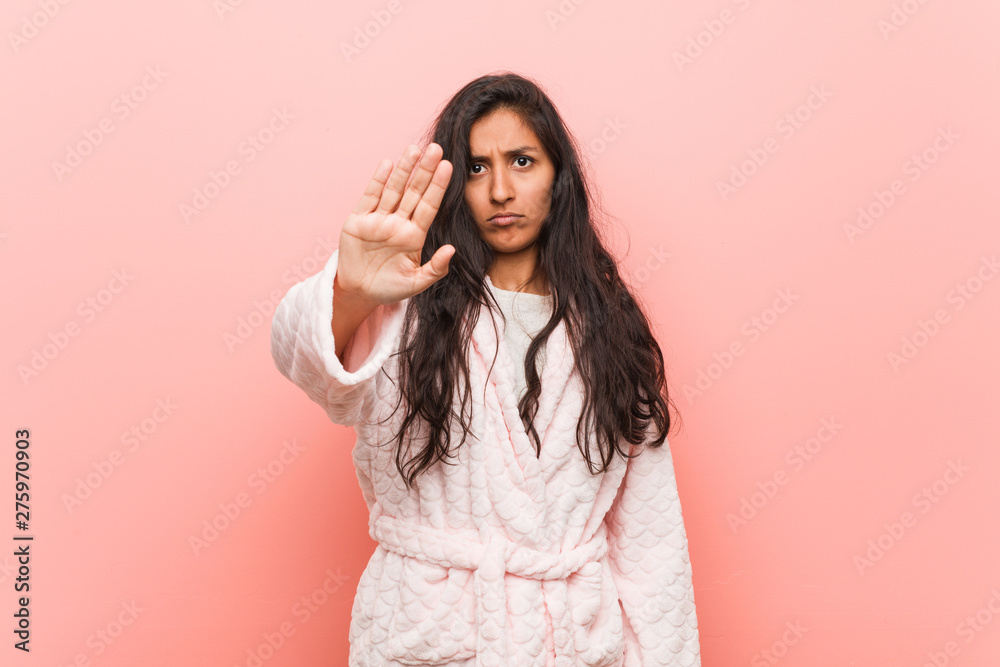 Young indian woman wearing pajama standing with outstretched hand showing stop sign, preventing you.