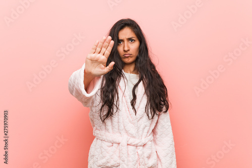 Young indian woman wearing pajama standing with outstretched hand showing stop sign, preventing you. © Asier