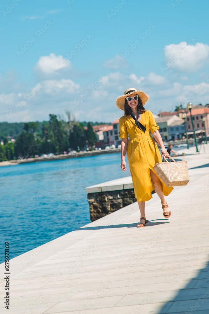 woman walking by sea quay in summer day in yellow sundress