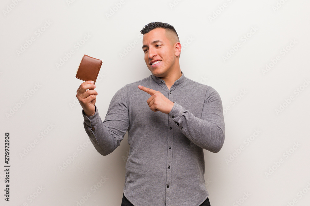 Young latin man holding a wallet pointing to the side with finger Young latin man holding a wallet pointing to the side with finger