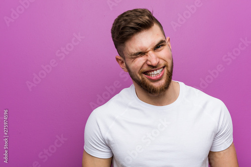 Young handsome caucasian man winking, funny, friendly and carefree.