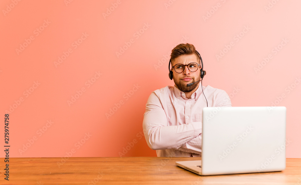 Young man working in a call center frowning face in displeasure, keeps arms folded.