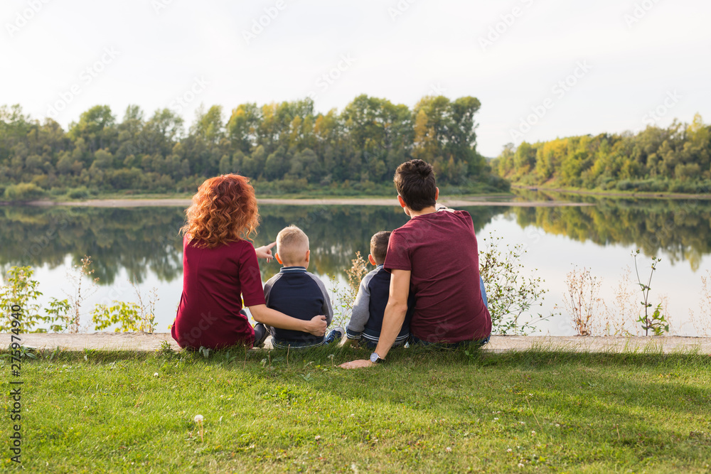 Parenthood, nature, people concept - family with two sons sitting near the lake Parenthood, nature, people concept - family with two sons sitting near the lake