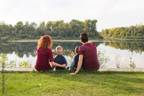 Parenthood, nature, people concept - family with two sons sitting near the lake