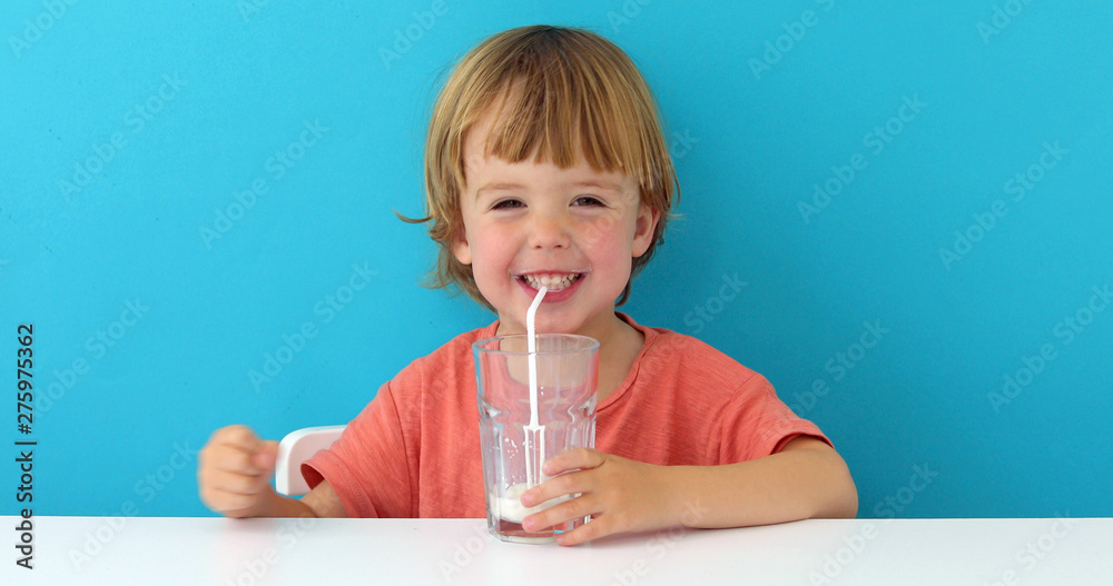 Little cute boy is drinking milk from a glass on blue background Little cute boy is drinking milk from a glass on blue background