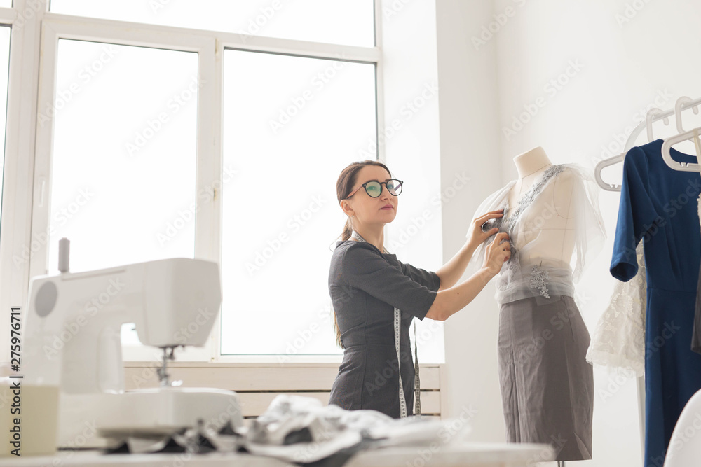 Obraz premium Dressmaker, tailor, fashion and showroom concept - Side view of female fashion designer measuring materials on mannequin in office