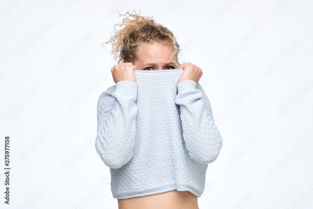 Caucasian girl with a social phobia hides her face in a sweater. She looks frightened around Caucasian girl with a social phobia hides her face in a sweater. She looks frightened around