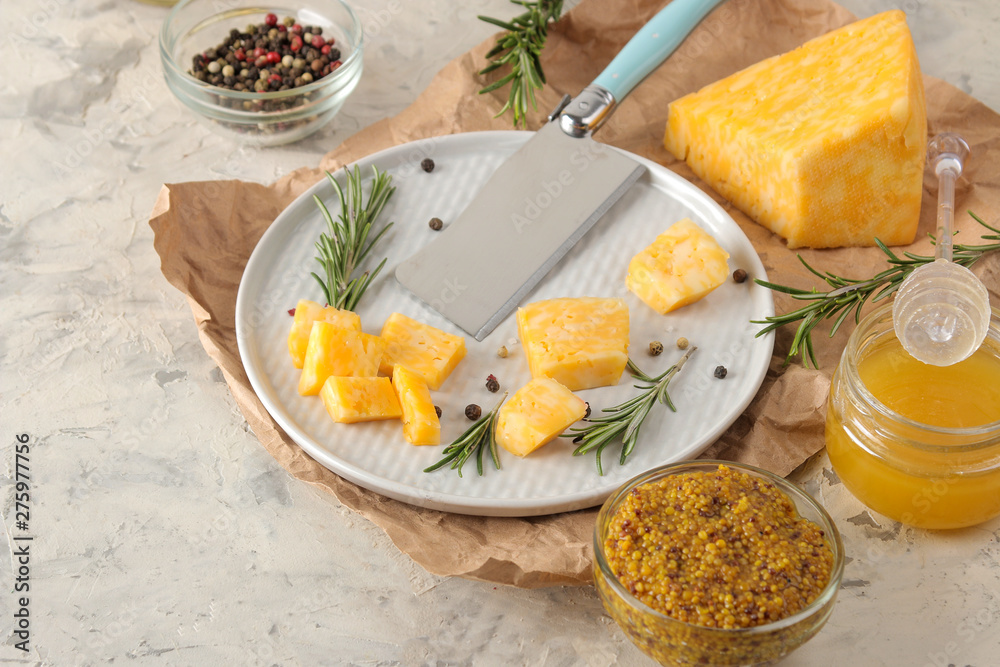 Slices of delicious marble cheese with a sprig of rosemary, honey and cheese knife on a plate on a light concrete background.