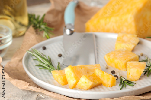 Slices of delicious marble cheese with a sprig of rosemary and cheese knife on a plate on a light concrete background. close-up