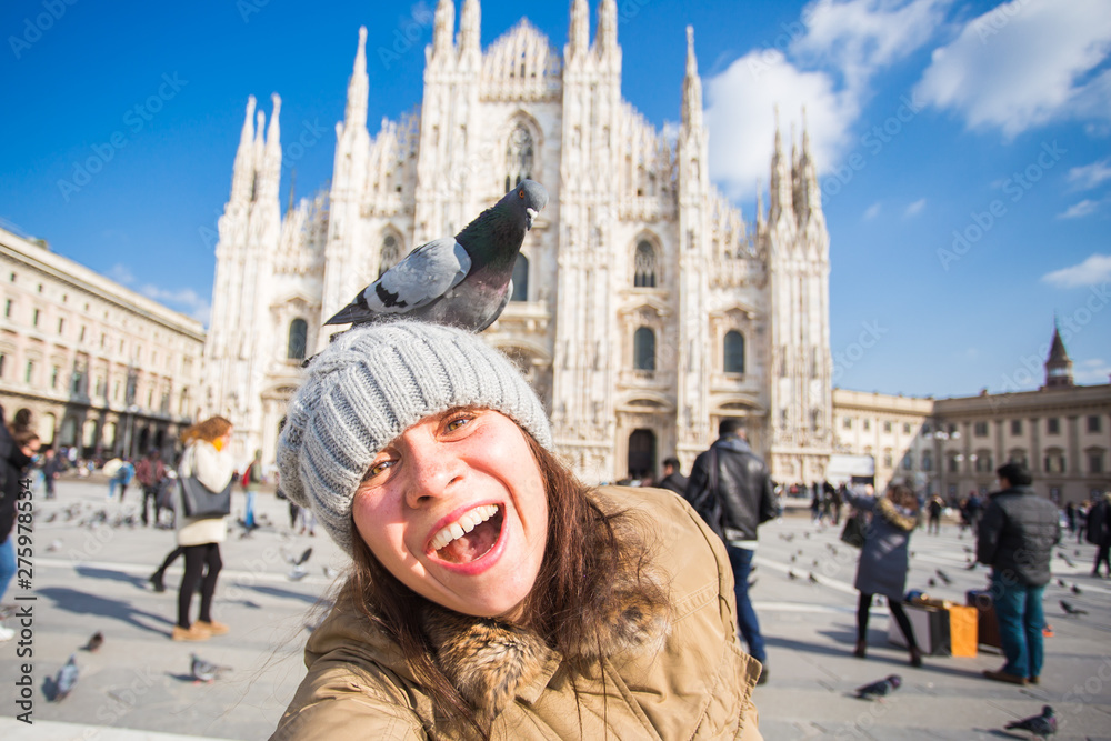 Italy, excursion and travel concept - young funny woman taking selfie with pigeons in front of cathedral Duomo in Milan