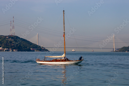 a small white sailing boat is anchored on Marmara Sea. You can see 3rd Bosphorus (Yavuz Sultan Selim) Bridge from Sariyer coast, Istanbul, Turkey photo