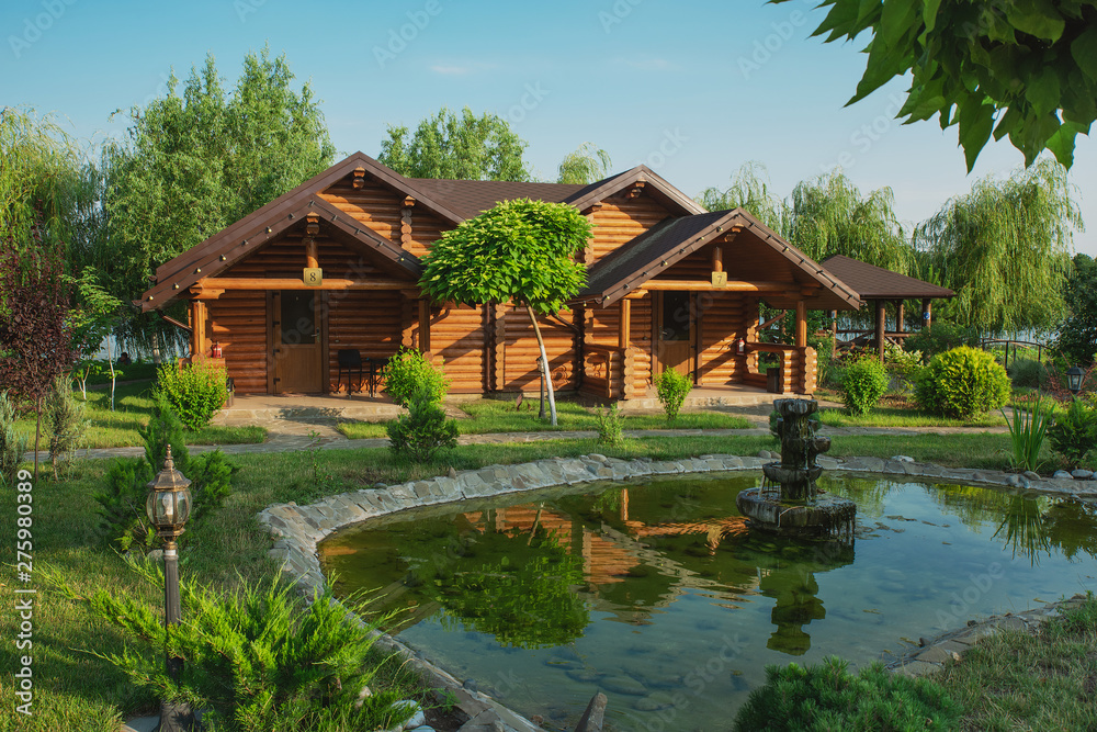 Wooden cottages with log and paved with wild stone paths on the background of green trees and flowering shrubs