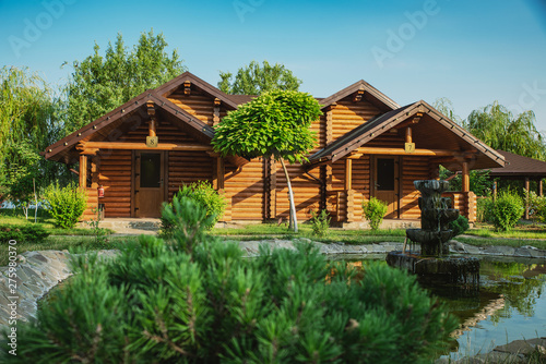 Wooden cottages with log and paved with wild stone paths on the background of green trees and flowering shrubs