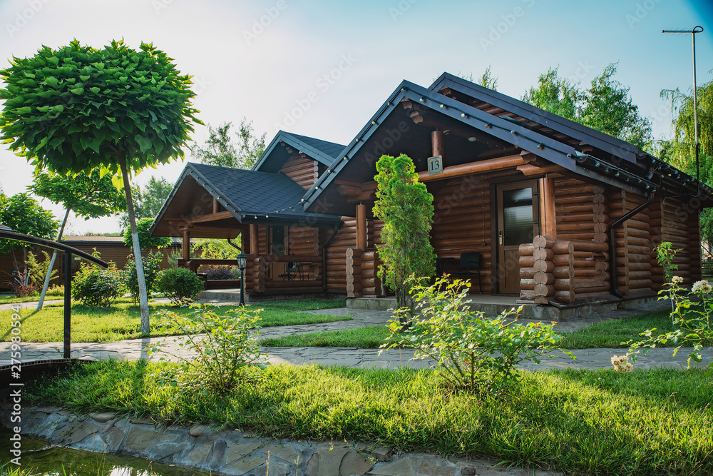 Wooden cottages with log and paved with wild stone paths on the background of green trees and flowering shrubs