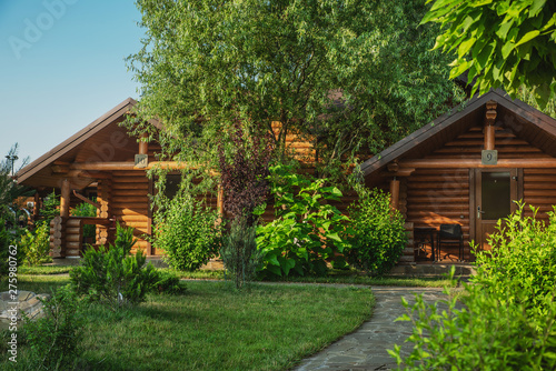 Wooden cottages with log and paved with wild stone paths on the background of green trees and flowering shrubs