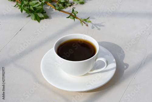 Fragrant coffee in a white cup, on a white table, with beautiful sprigs of leaves. photo
