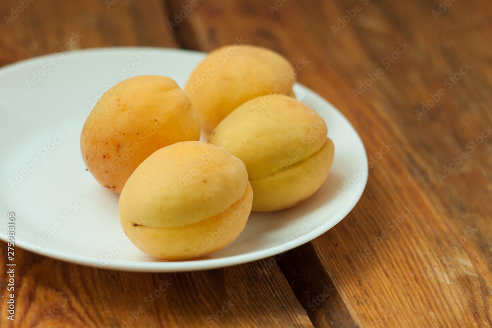 Ripe fresh apricot fruits on a white plate on the wooden background. Copy space, delisious healthy food.
