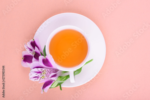 Beautiful flowers of astromeria. Herbal tea in a white cup and a white saucer on a pink background