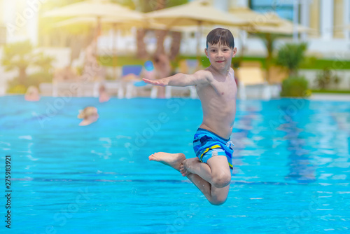 Caucasian boy having fun making fantastic jump into swimming pool at resort.  He is enjoying his summer vacations. © Artem