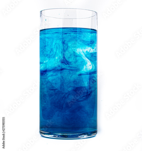 Blue food coloring diffuse in water inside glass with empty copyspace area for slogan or advertising text message, over isolated white background.