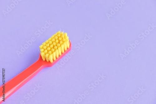 Red plastic toothbrush with bright yellow bristles with selective focus on blurred purple background with empty space for text. Toothbrush for daily cleaning of teeth and caries protection 