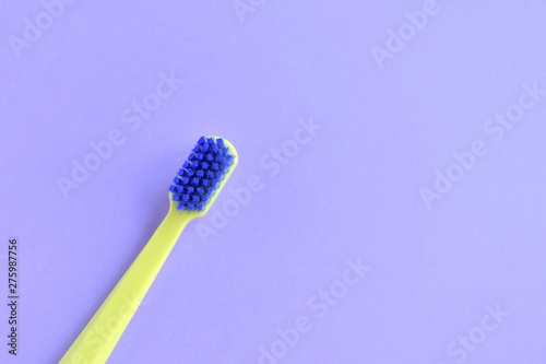 Neon green p plastic toothbrush with blue bristles with selective focus on blurred purple background with empty space for text. Toothbrush for daily cleaning of teeth and caries protection 