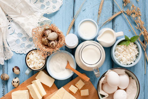 Different types of dairy products on blue wooden background: milk, sour cream, cottage cheese, cheese, cream, yogurt, eggs and butter top view with copy space