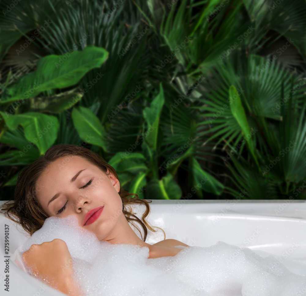 A woman relaxes in hot bath tub with soap foam