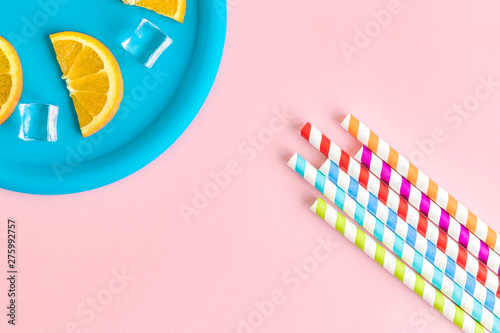 Orangeade abstract made of colorful drinking straws and orange fruit slices with ce cubes on plate isolated on rose.
