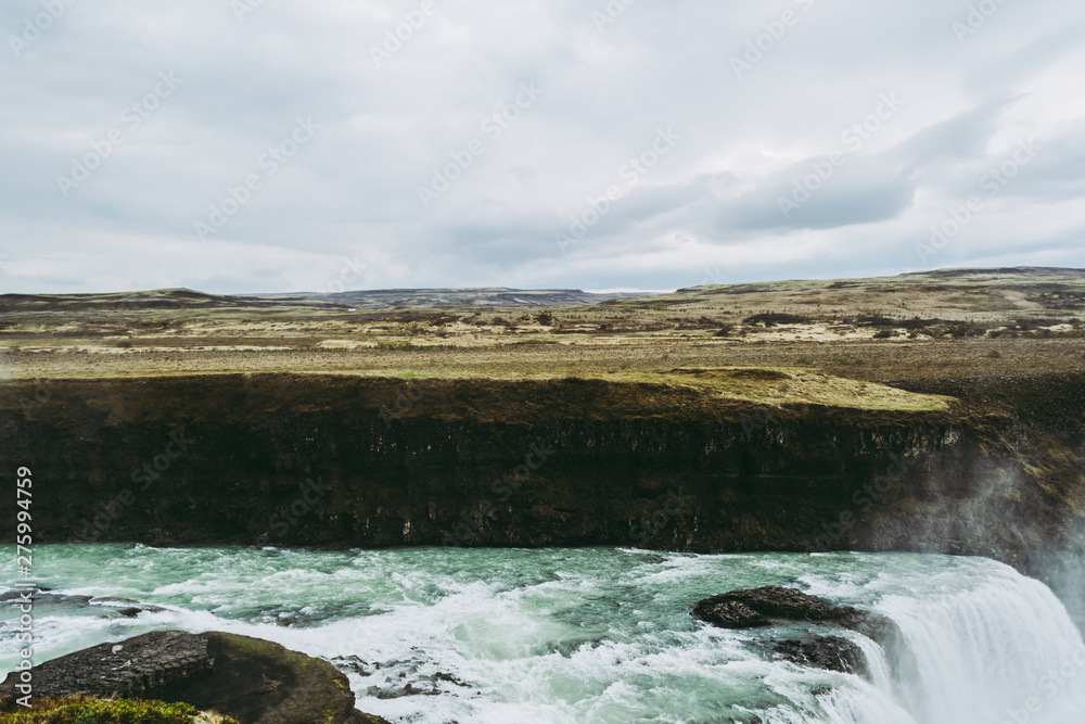 Horizontal view of Gullfoss waterfall in Southwest Iceland. Blue and green water with pale white splashes flying over it. Icelandic landscapes.