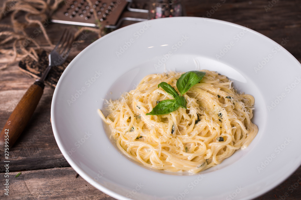 Delicious creamy Italian spaghetti pasta starter with cheese and fresh basil on rustic wooden table