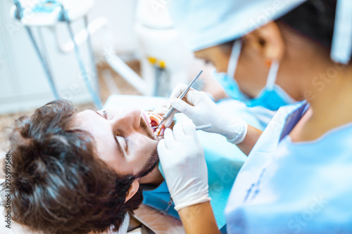 Giovane ragazza dentista sta visitando un paziente ragazzo con barba sulla poltrona. photo