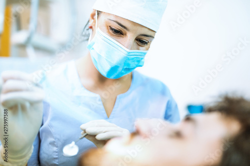 Giovane ragazza dentista sta visitando un paziente ragazzo con barba sulla poltrona. photo