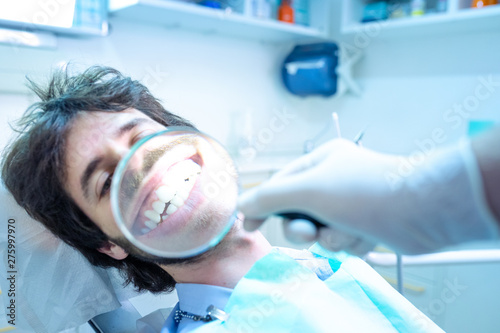 Giovane ragazzo seduto sulla poltrona del dentista, fa vedere il suo stupendo sorriso con la lente d'ingrandimento. Dopo aver tolto l'apparecchio ai denti. photo