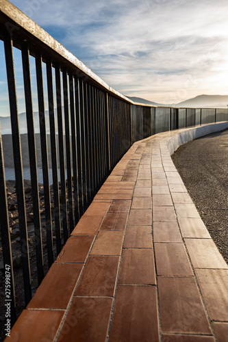 Metallic and wooden railing on a coast cliff illuminated by the sunset light
