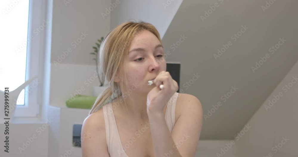 Blond woman brushing her teeth in bathroom. Everyday routine.