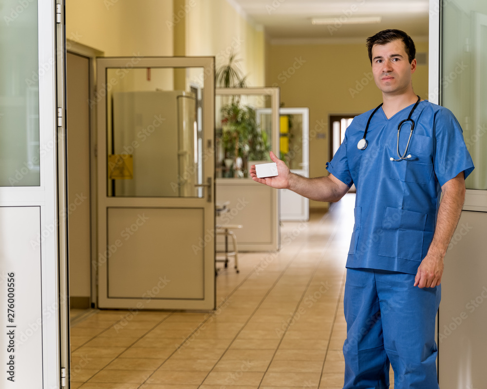 Middle age male doctor in blue scrubs with stethoscope holding White Card Middle age male doctor in blue scrubs with stethoscope holding White Card