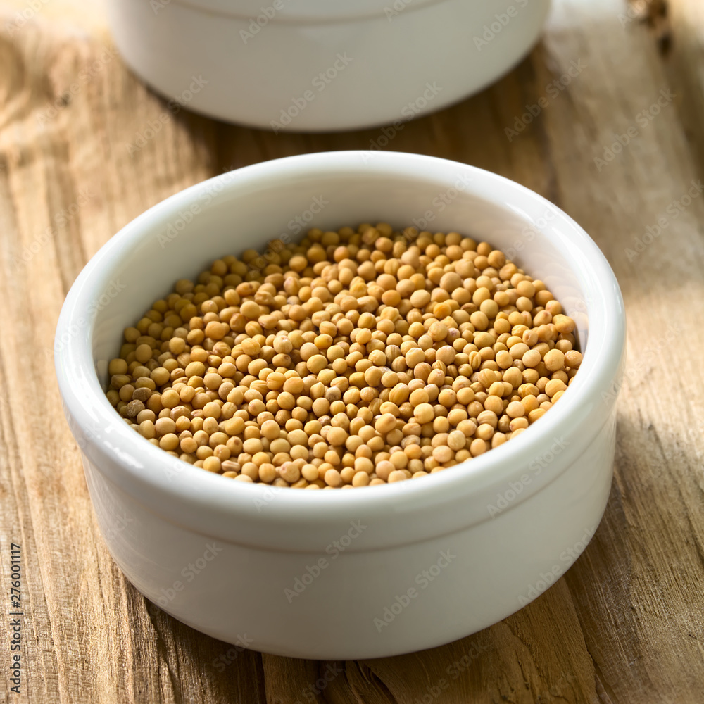 Yellow mustard seeds in small bowl, photographed on wood with natural light (Selective Focus, Focus one third into the seeds) Yellow mustard seeds in small bowl, photographed on wood with natural light (Selective Focus, Focus one third into the seeds)