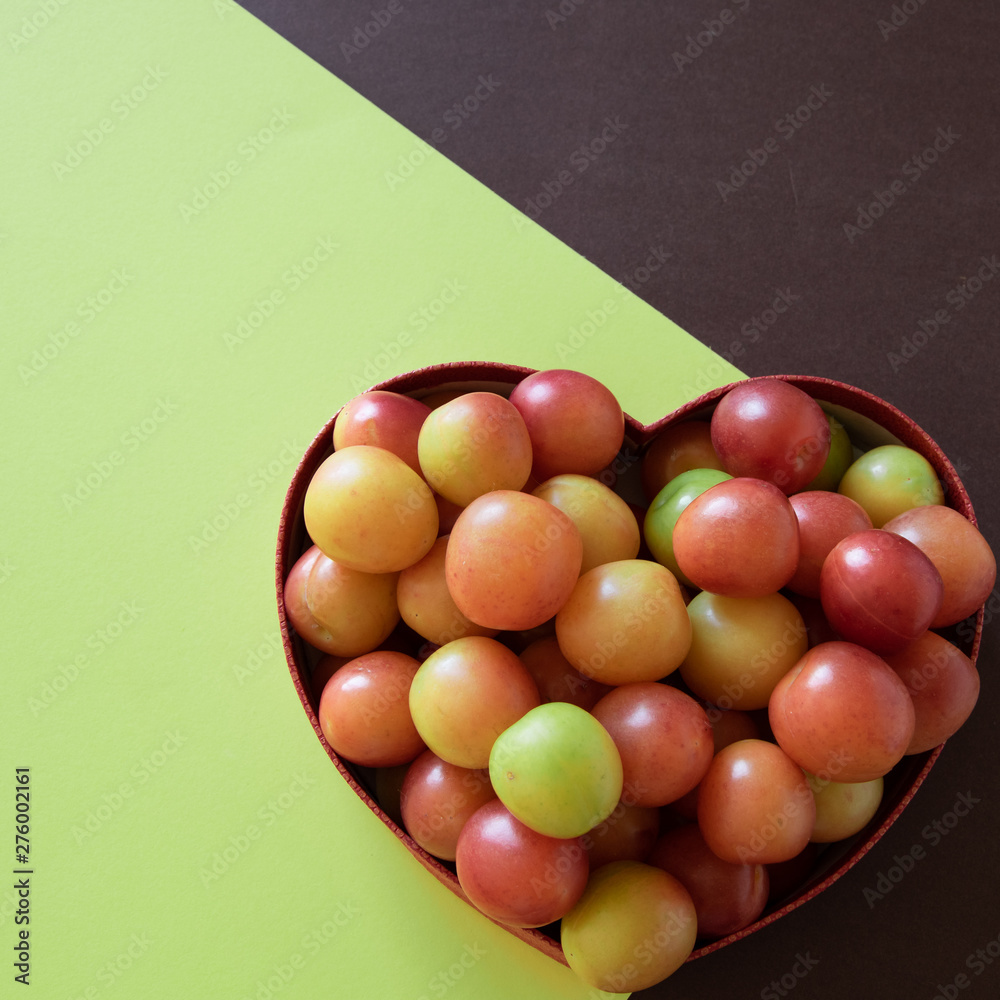 Obraz premium Organic fresh plums in heart shape box on geometric background. Healthy vegetarian food. Still life with space for text.