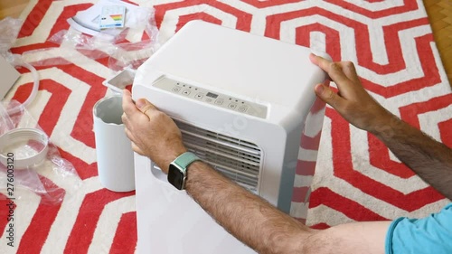Young man unboxing installing new portable air conditioner unit AC during hot summer in his living room inspection