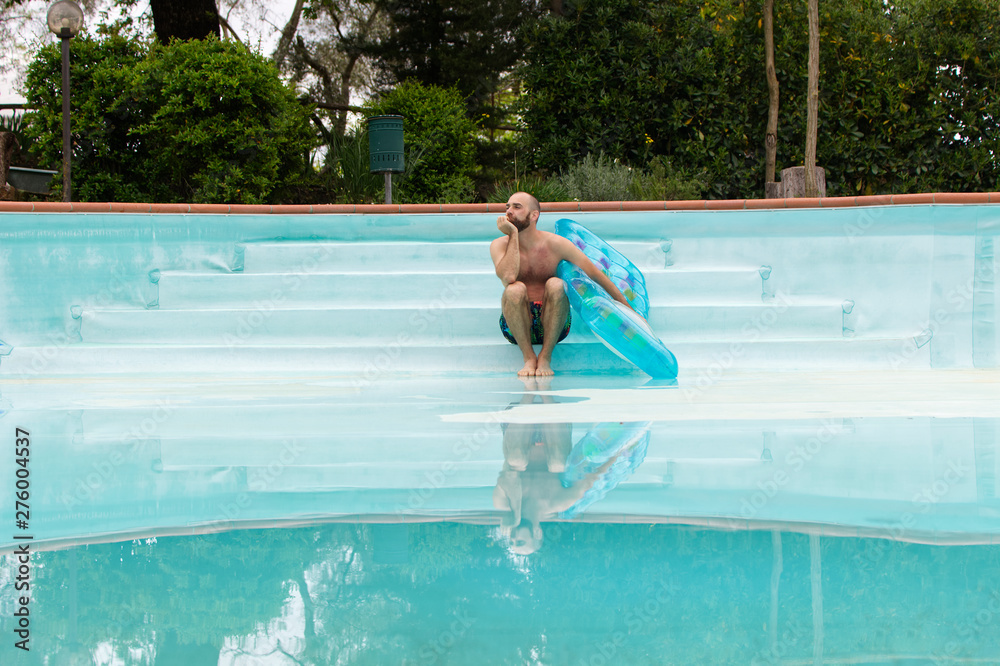 Badegast mit einer Luftmatratze am leeren Schwimmbecken